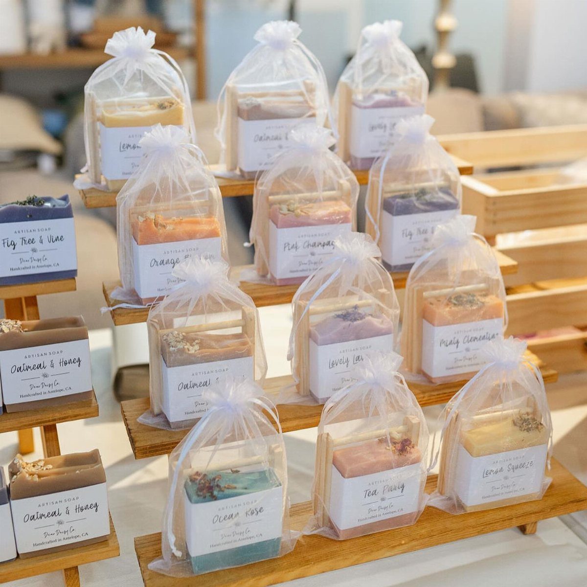 Artisanal soap bars in clear plastic packaging displayed on wooden tiered shelves.