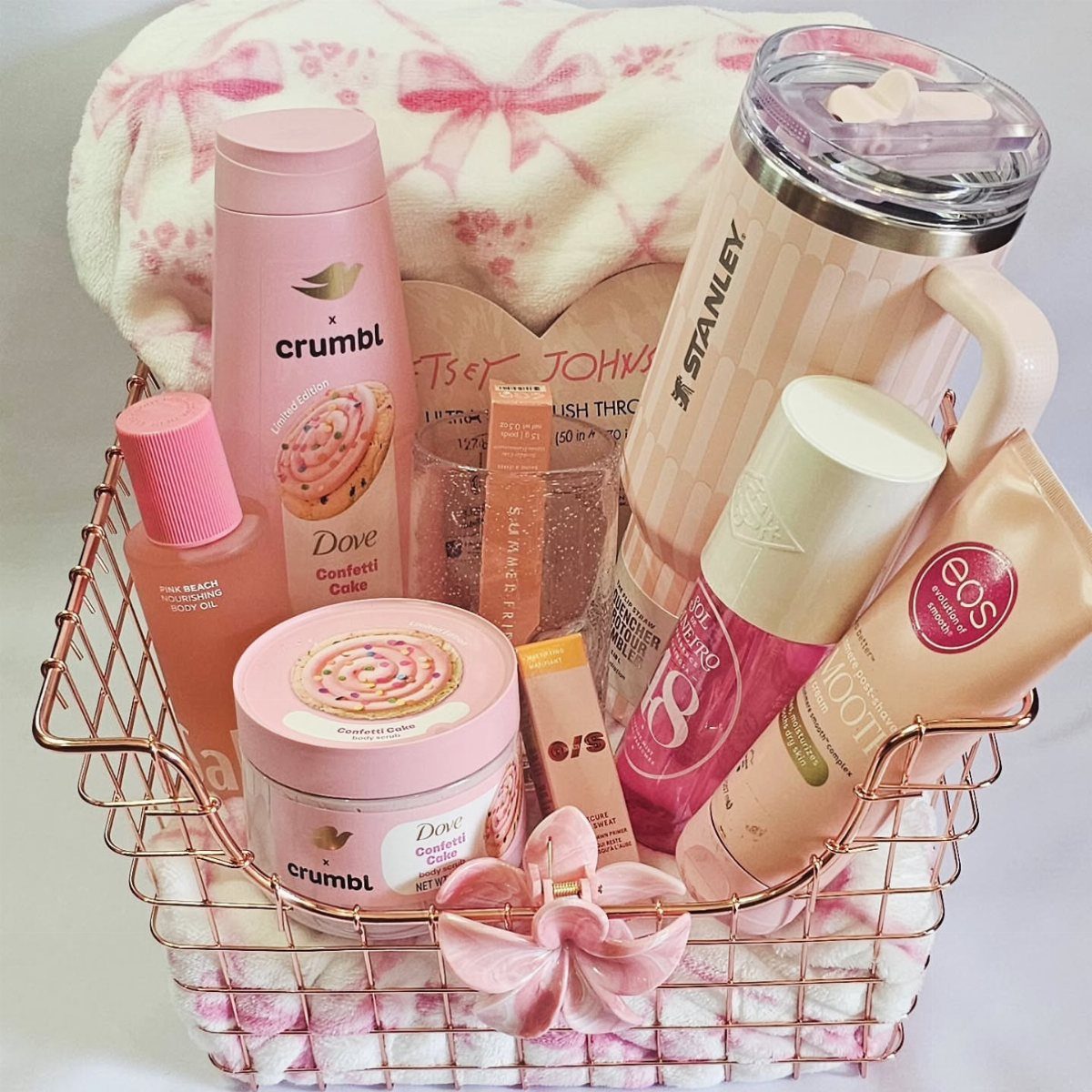 Rose gold basket filled with pink Dove beauty products, Stanley tumbler, and plush blanket.