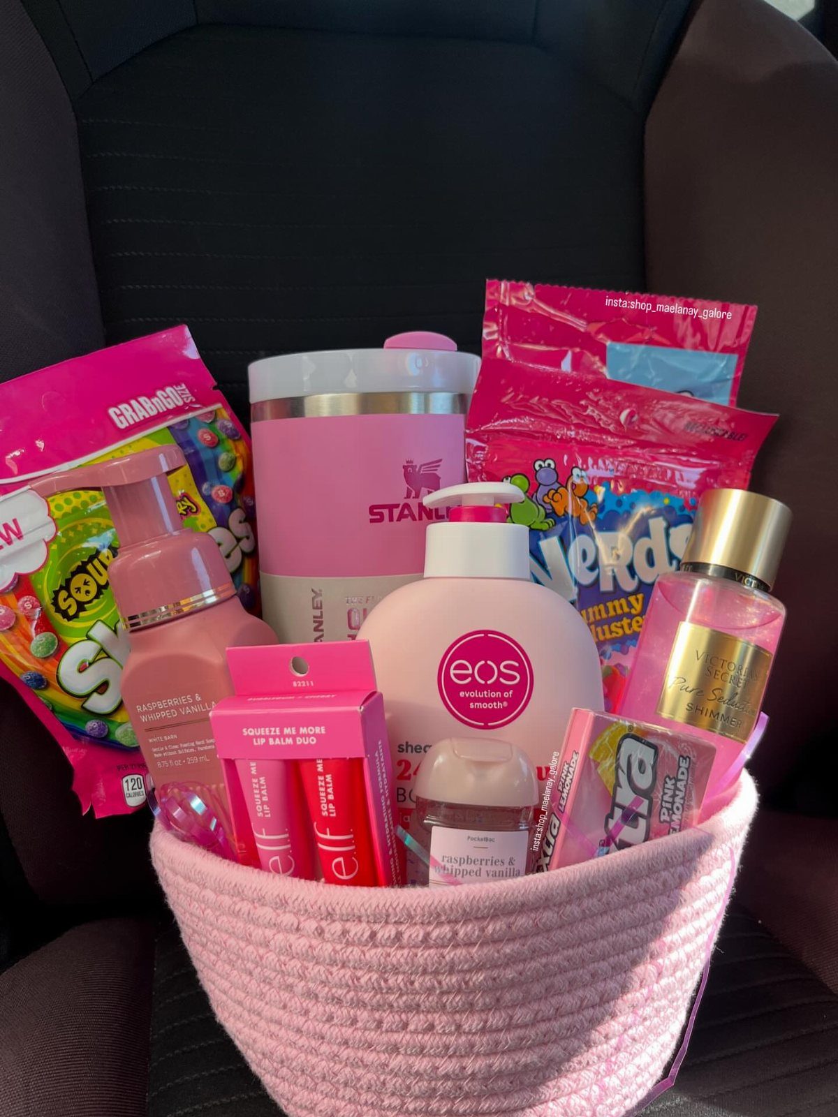 Pink woven basket filled with pink beauty products, candy, and a Stanley tumbler.