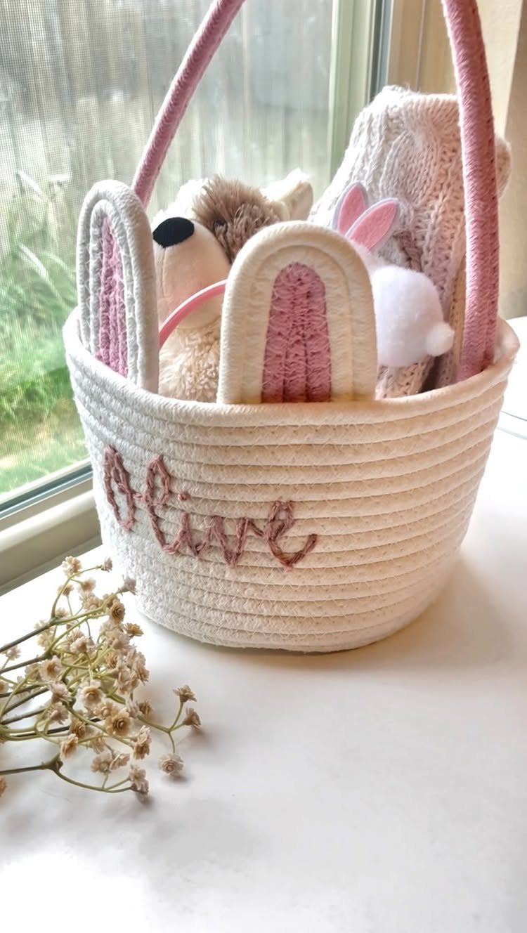 White rope basket with pink handles filled with plush toys and a blanket.