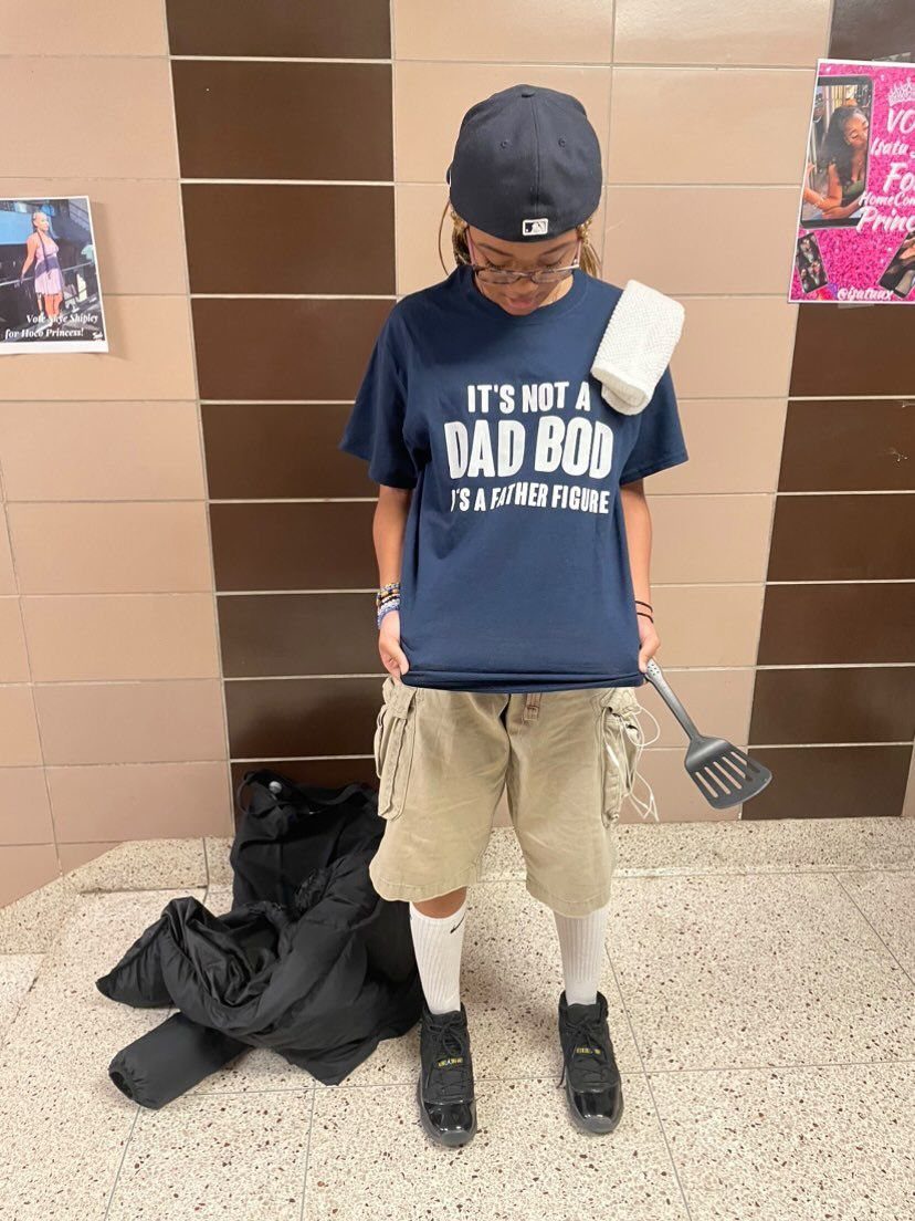 Person in a BBQ dad costume wearing a black baseball cap and cargo shorts.
