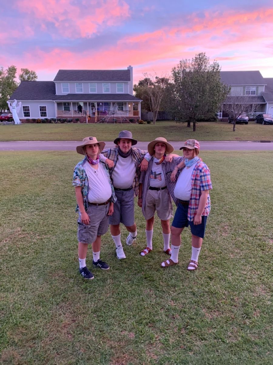 Four people in BBQ dad costumes with fake bellies posing on a lawn.