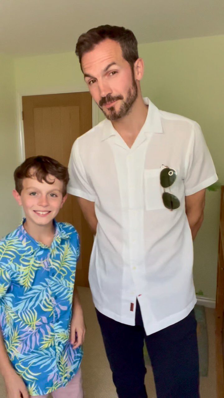 Boy in a blue floral button-down shirt standing next to a man in white.