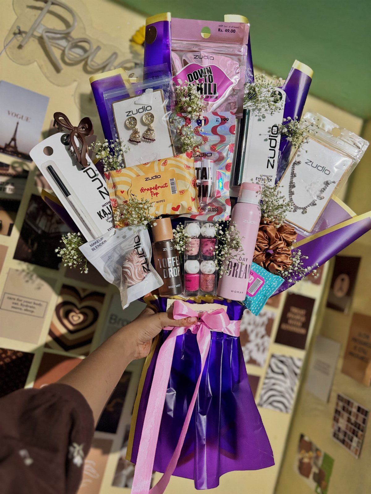 Gift bouquet in purple wrapping containing jewelry and beauty products with white flowers.