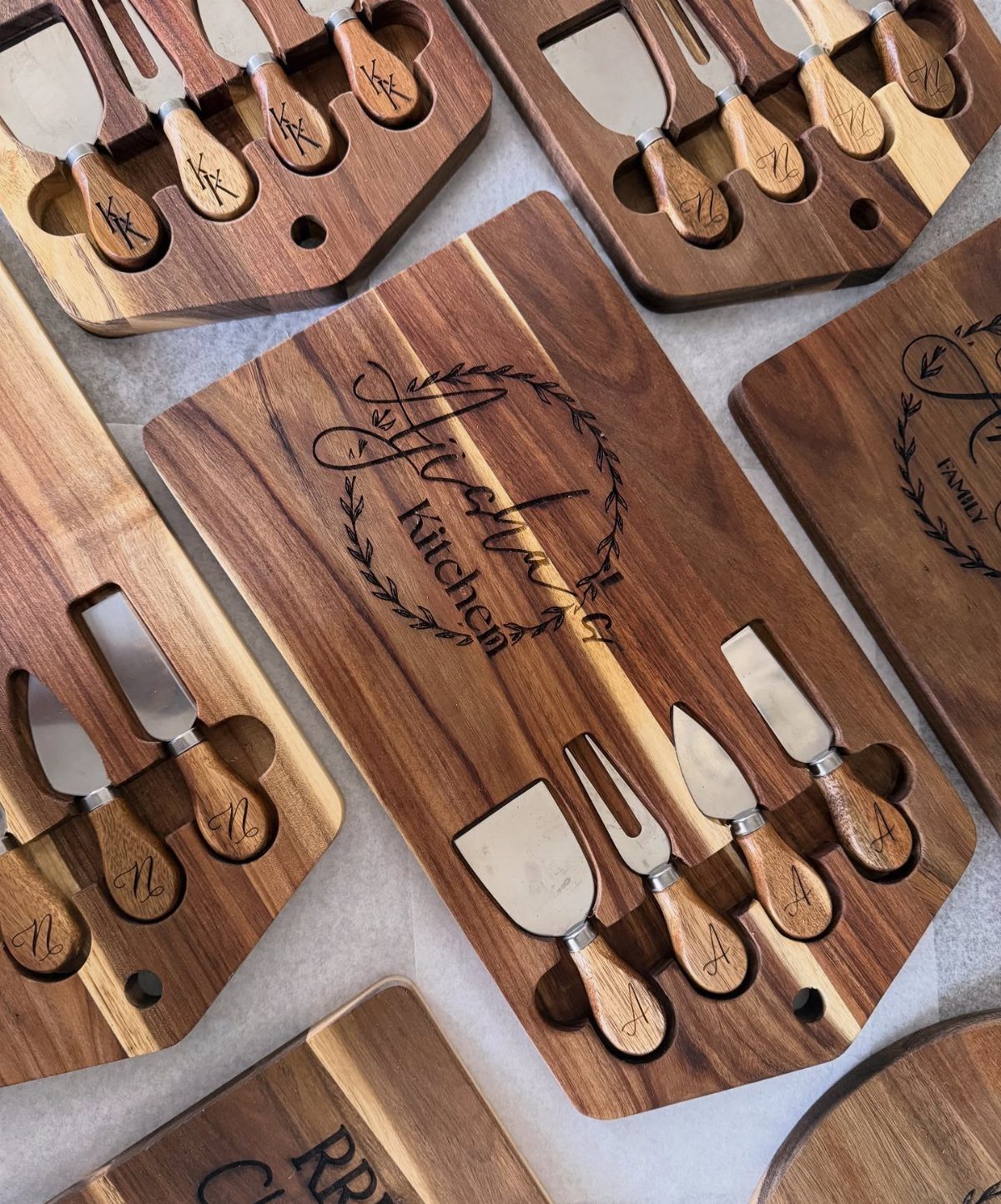 Wooden charcuterie boards with engraved text and matching cheese knives on a light surface.