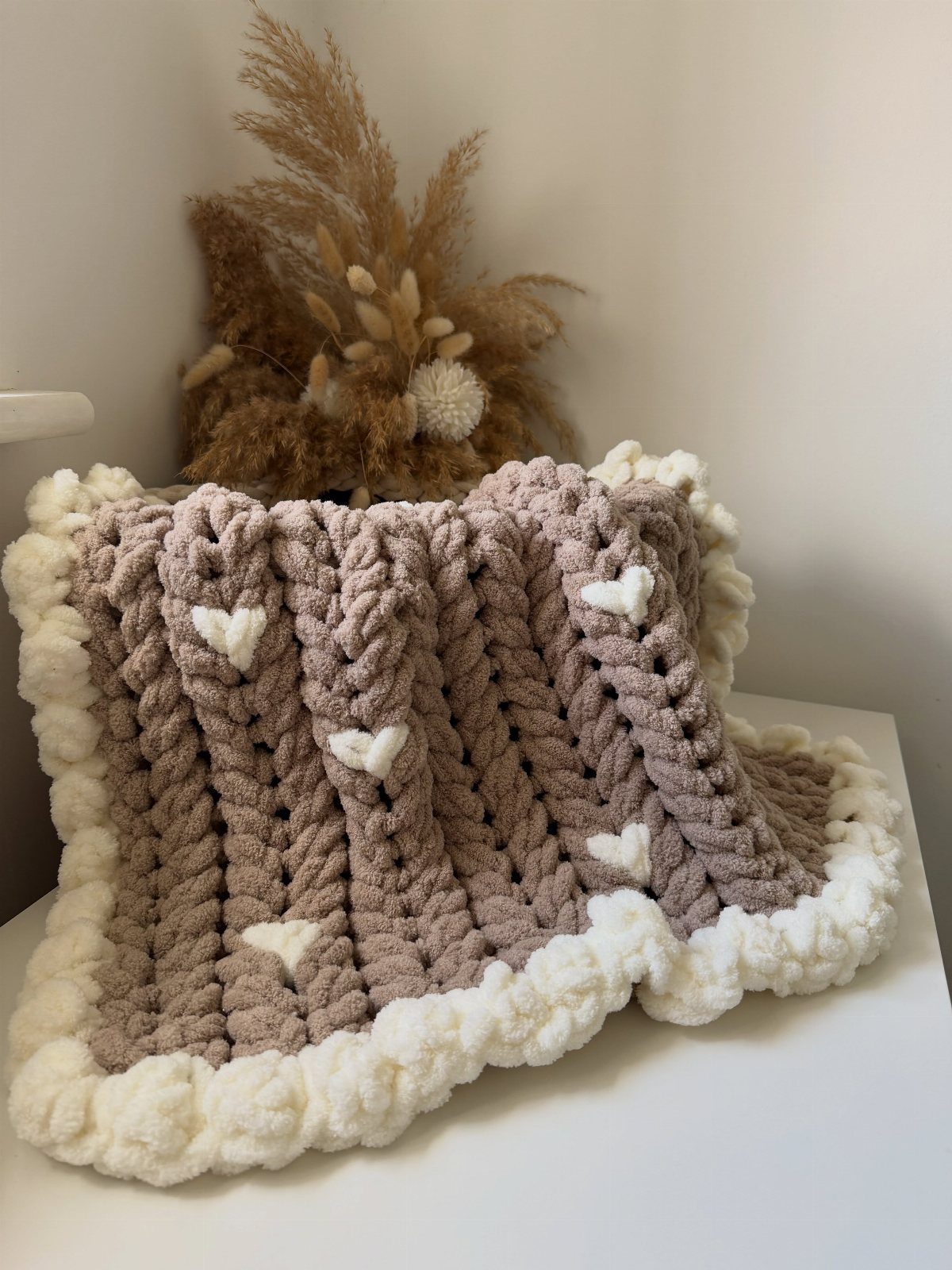 Chunky knit mauve throw blanket with white hearts and a cream border.