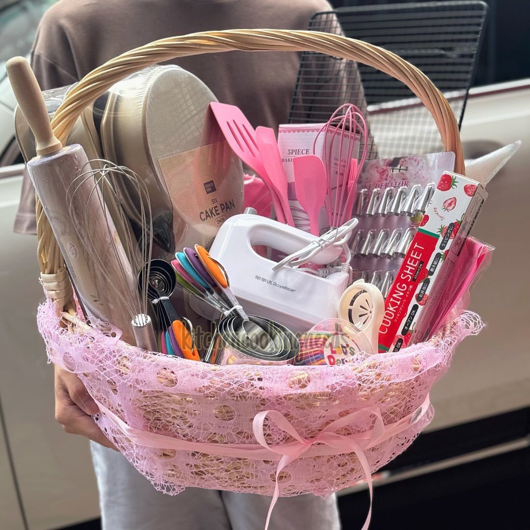 Baking gift basket with pink lace, containing a hand mixer and various kitchen tools.