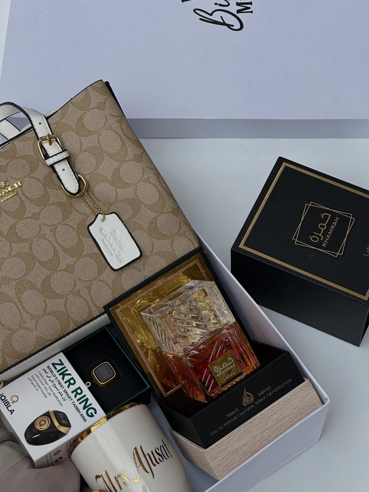 Gift box with beige handbag, perfume, Zikr ring, and a white mug.