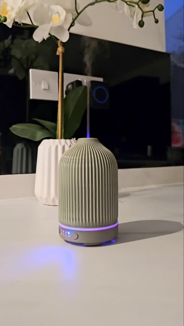 Ribbed light green essential oil diffuser emitting mist with a purple glowing base.
