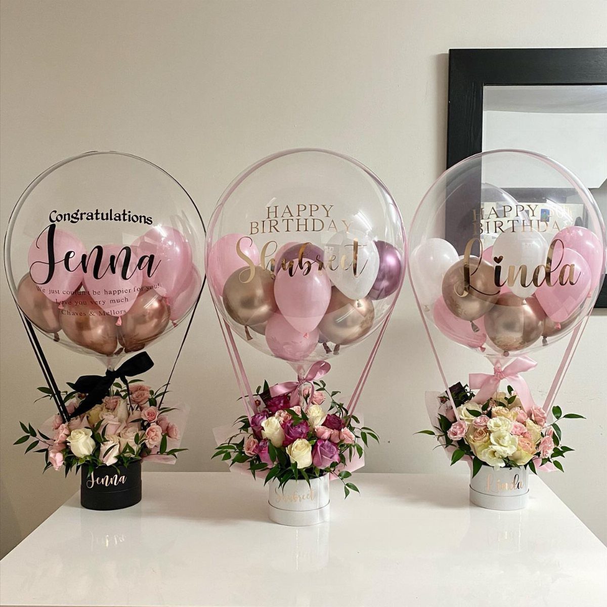 Three hot air balloon gift arrangements with pink roses and personalized balloons.