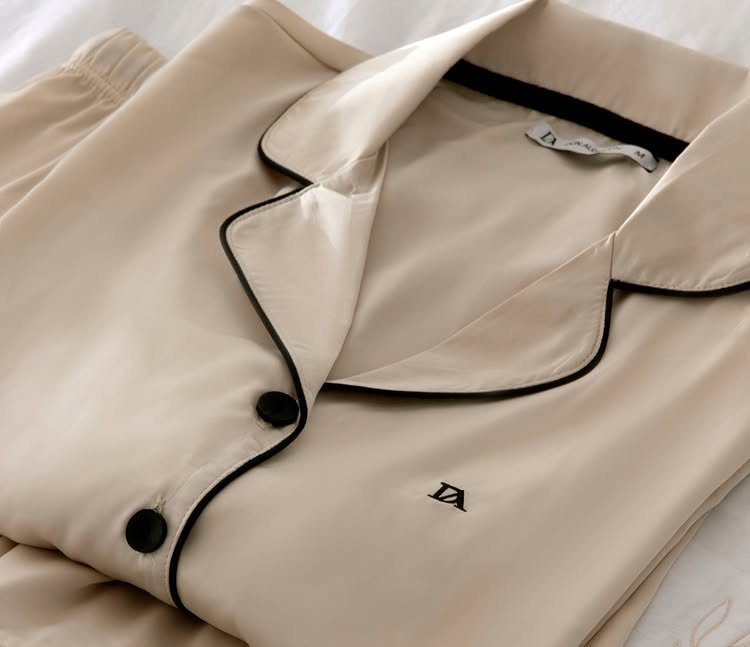 Cream satin pajama set with black piping and buttons on white bedding