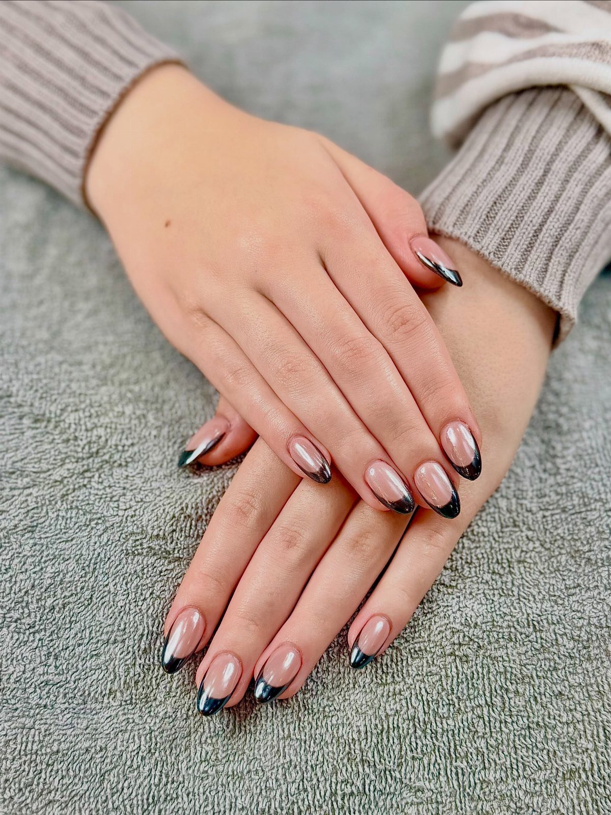 Almond-shaped nails with nude base and metallic black chrome French tips on hands.