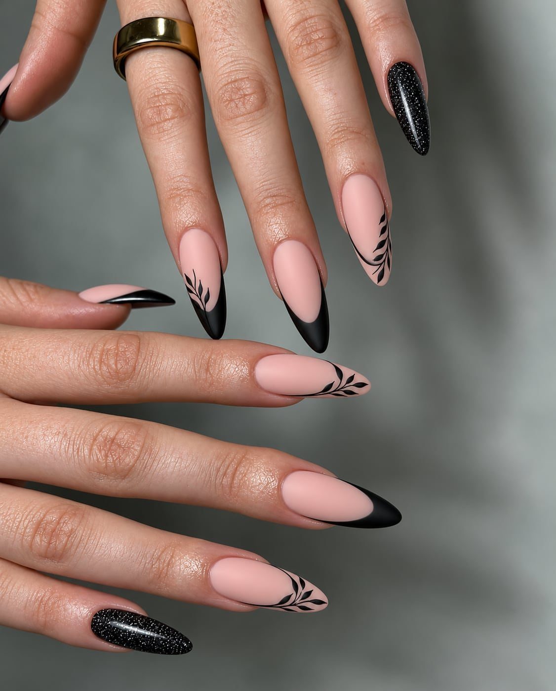 Almond-shaped nails with nude base, black French tips, leaf accents, and black glitter.