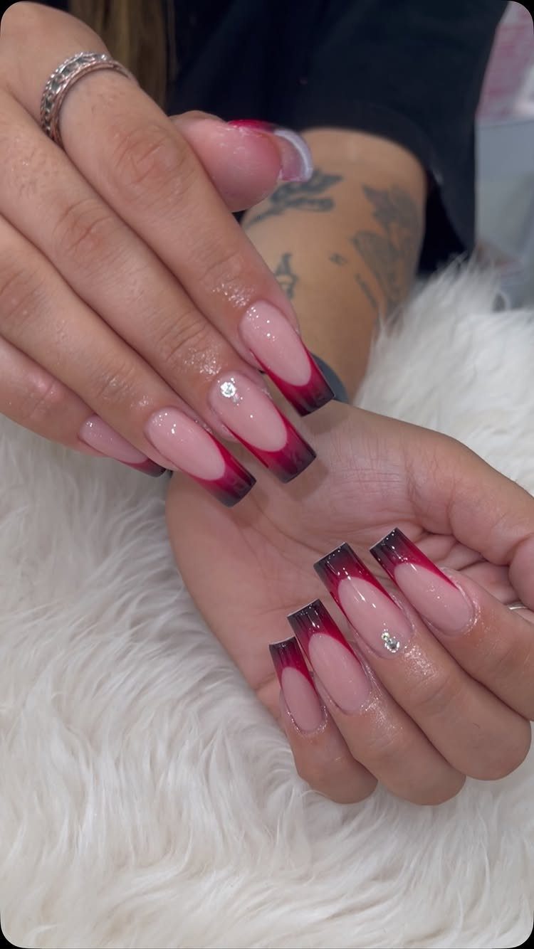 Long coffin nails with a red and black gradient French tip and rhinestones.