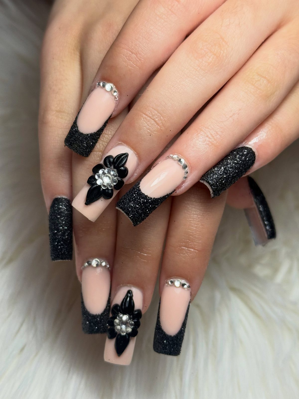 Nude nails with black glitter French tips and rhinestone floral accents