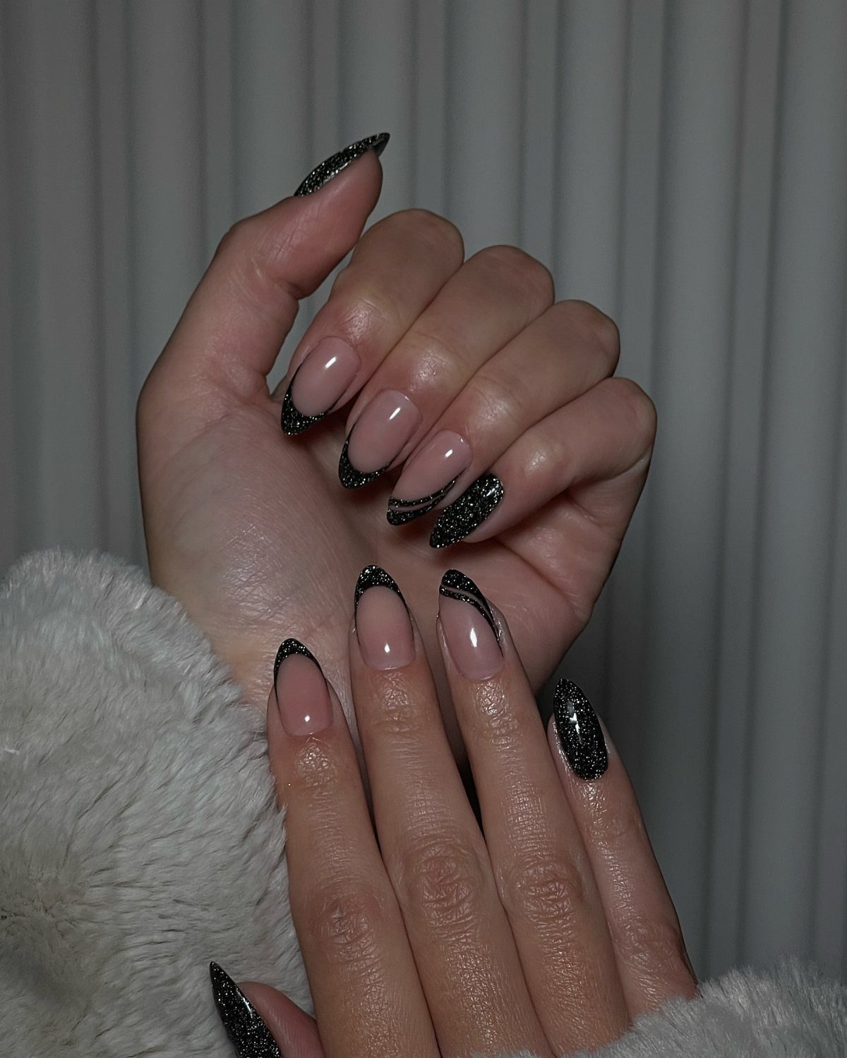 Almond-shaped nails with nude base and black glitter French tips on hands.