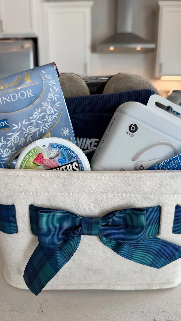 White fabric gift basket with blue plaid bow containing headphones and blue packaging.