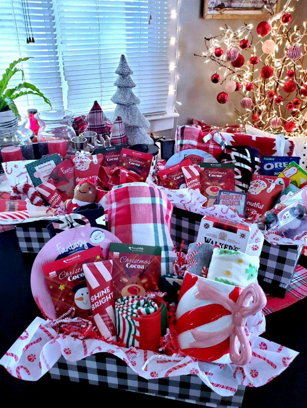 Festive holiday gift basket with cocoa, a striped mug, and red plaid accents.