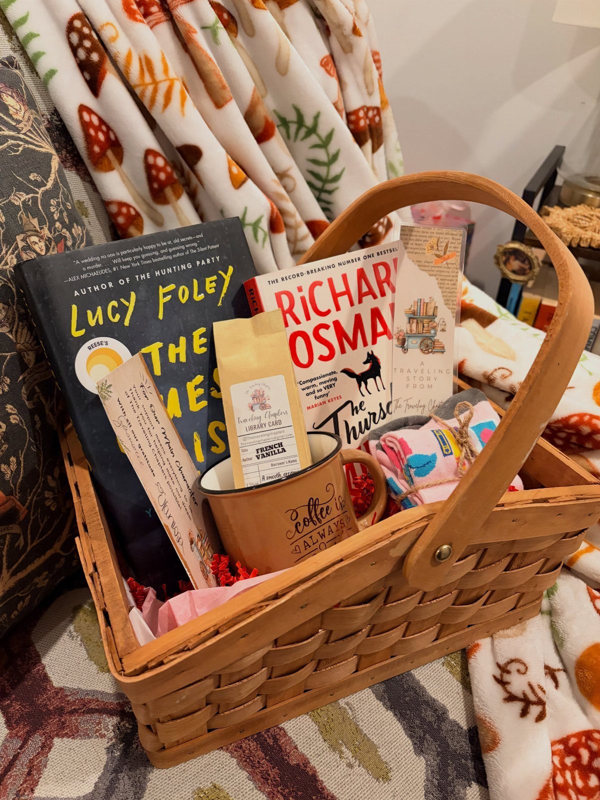 Woven gift basket containing books, a ceramic mug, and coffee on patterned blankets.