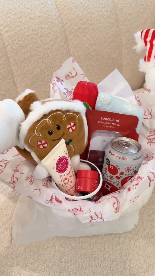 Gift basket with gingerbread plush, cranberry drink, and skincare products in tissue paper.