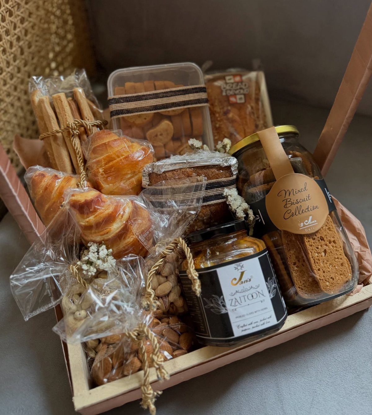 Gift basket with croissants, biscuits, almonds, and Zaitoon spread in a wooden tray.
