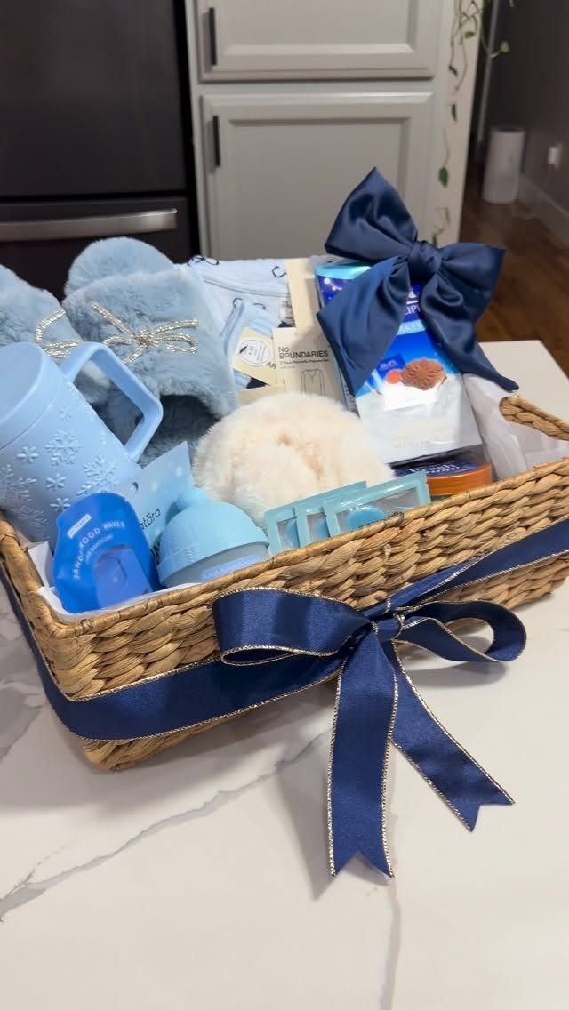 Woven gift basket with blue slippers, mug, and skincare products tied with navy ribbon.