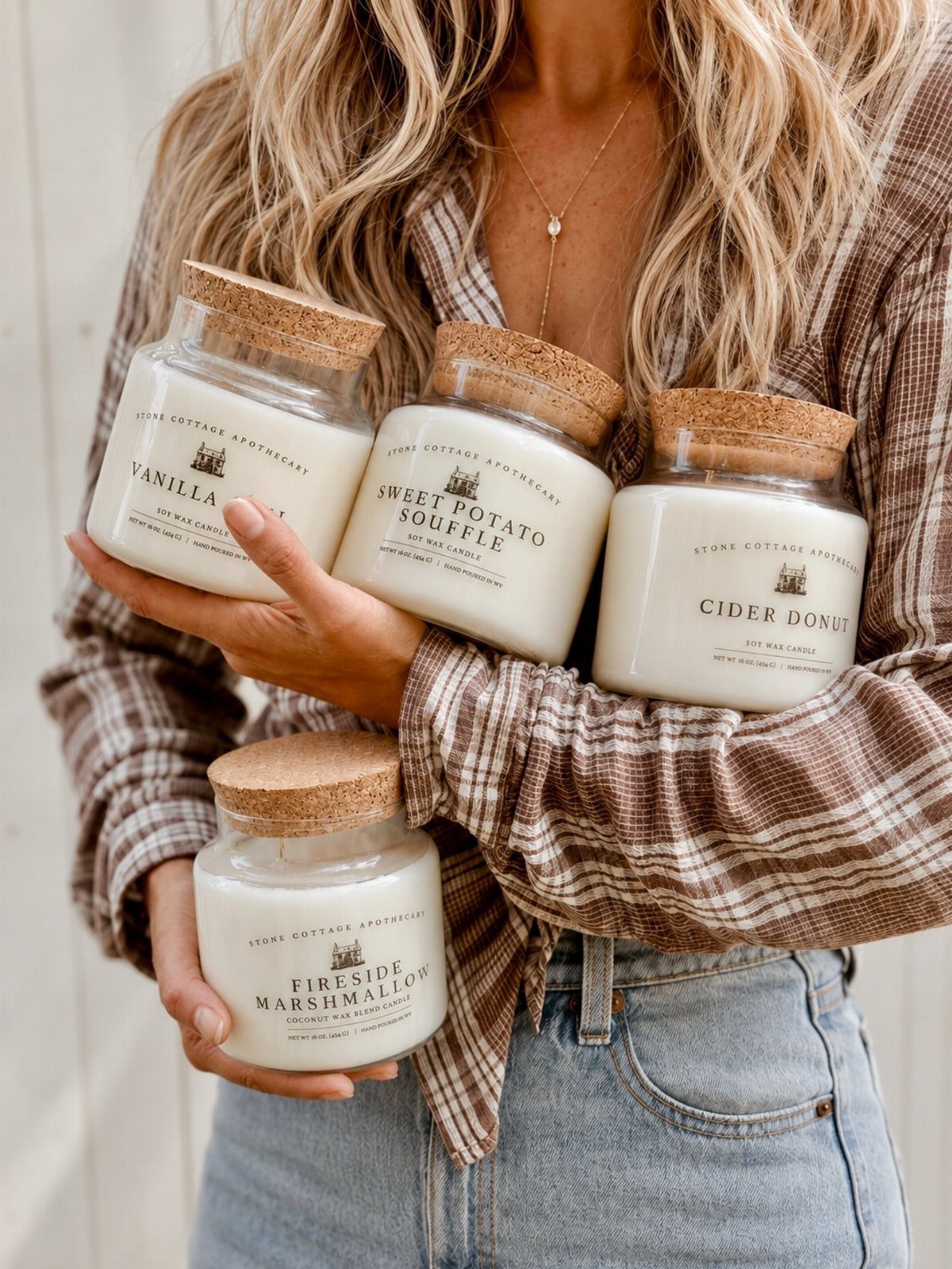 Four white scented candles in glass jars with cork lids held by a person.