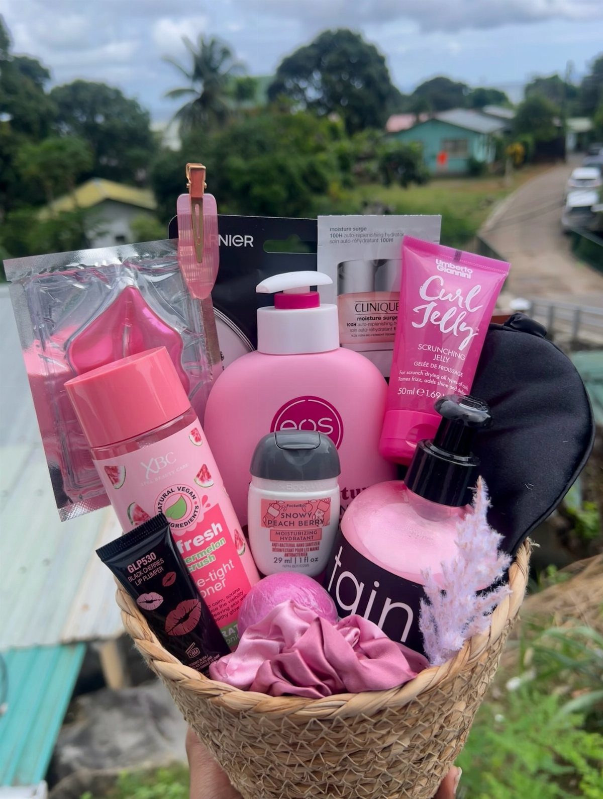 Woven gift basket filled with pink skincare products and beauty accessories outdoors.