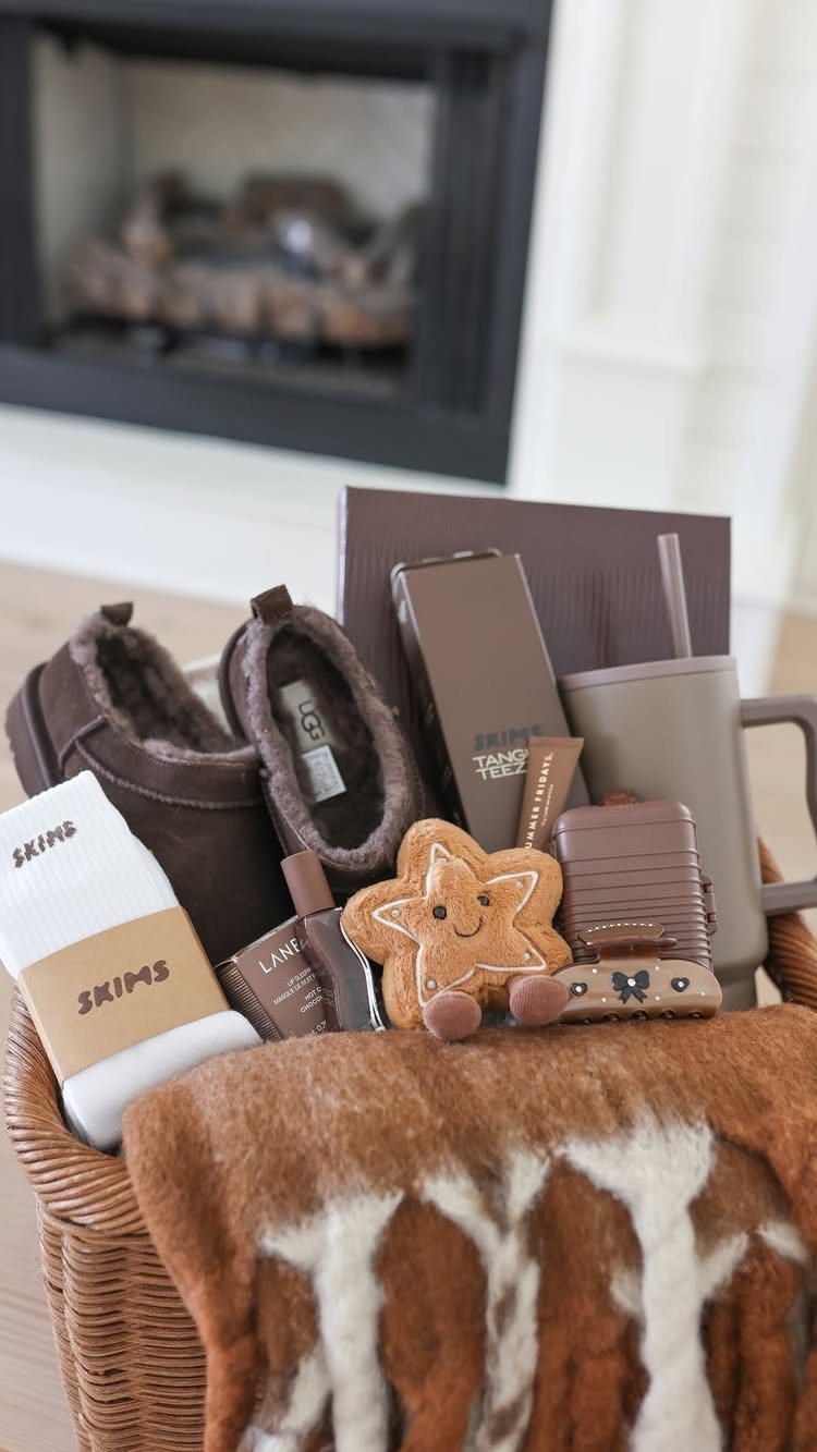 Wicker gift basket containing brown boots, a mug, and a cozy blanket.