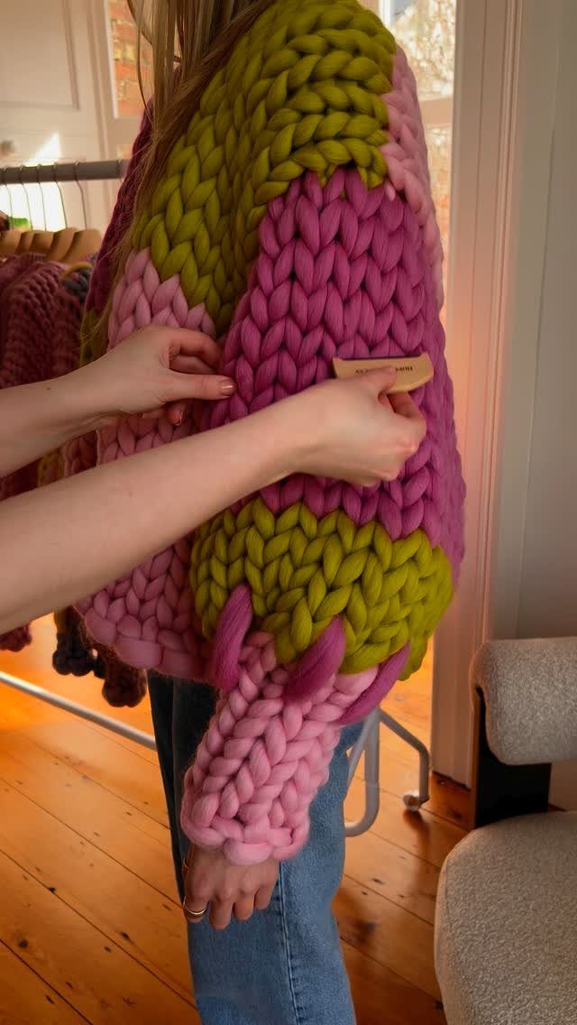 Person wearing a chunky pink and olive green knit cardigan with blue jeans.