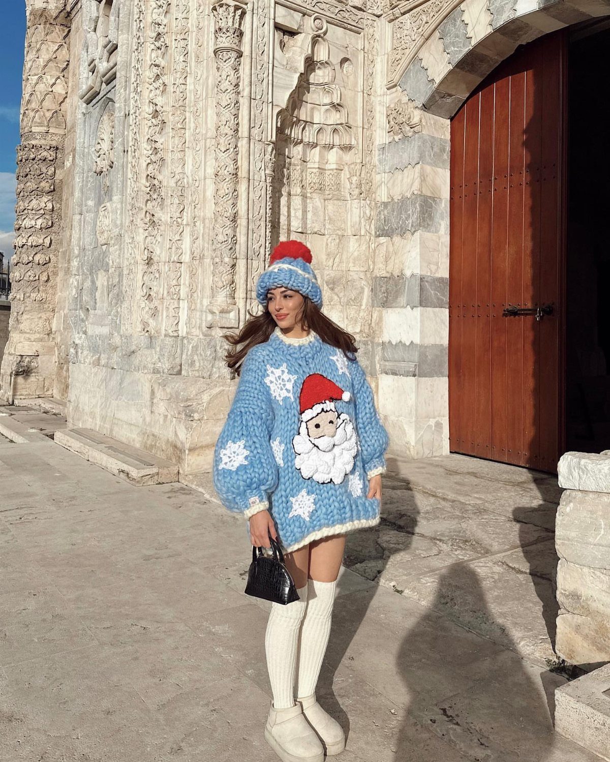 Woman wearing a blue Santa knit sweater, blue beanie, and white knee-high socks.