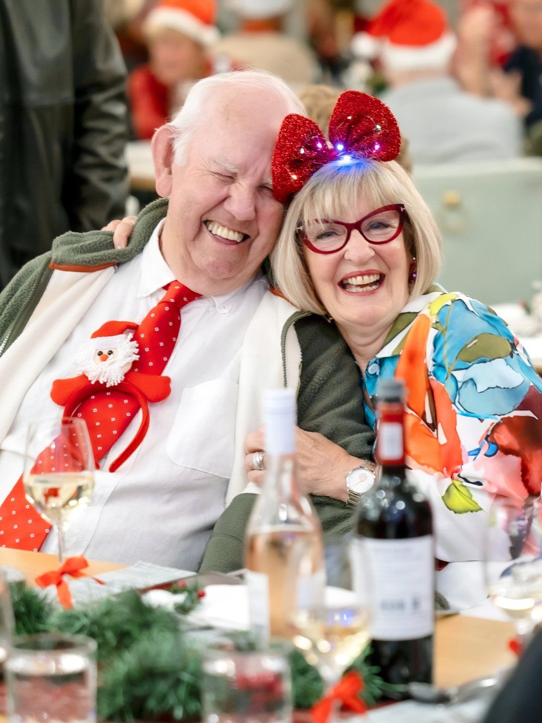 Older couple smiling, man wearing a red polka-dot tie with a snowman decoration.