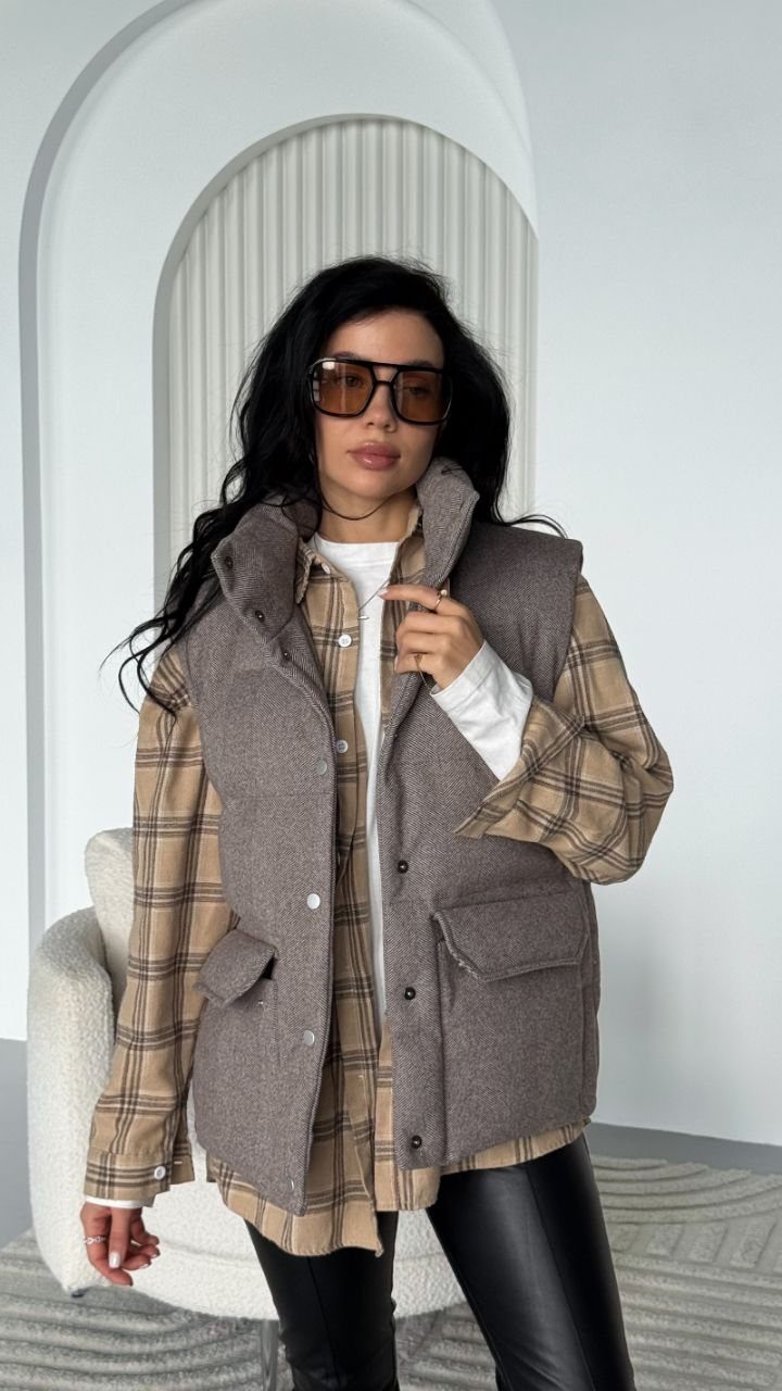 Woman wearing a brown plaid shirt, grey vest, and black leather pants.