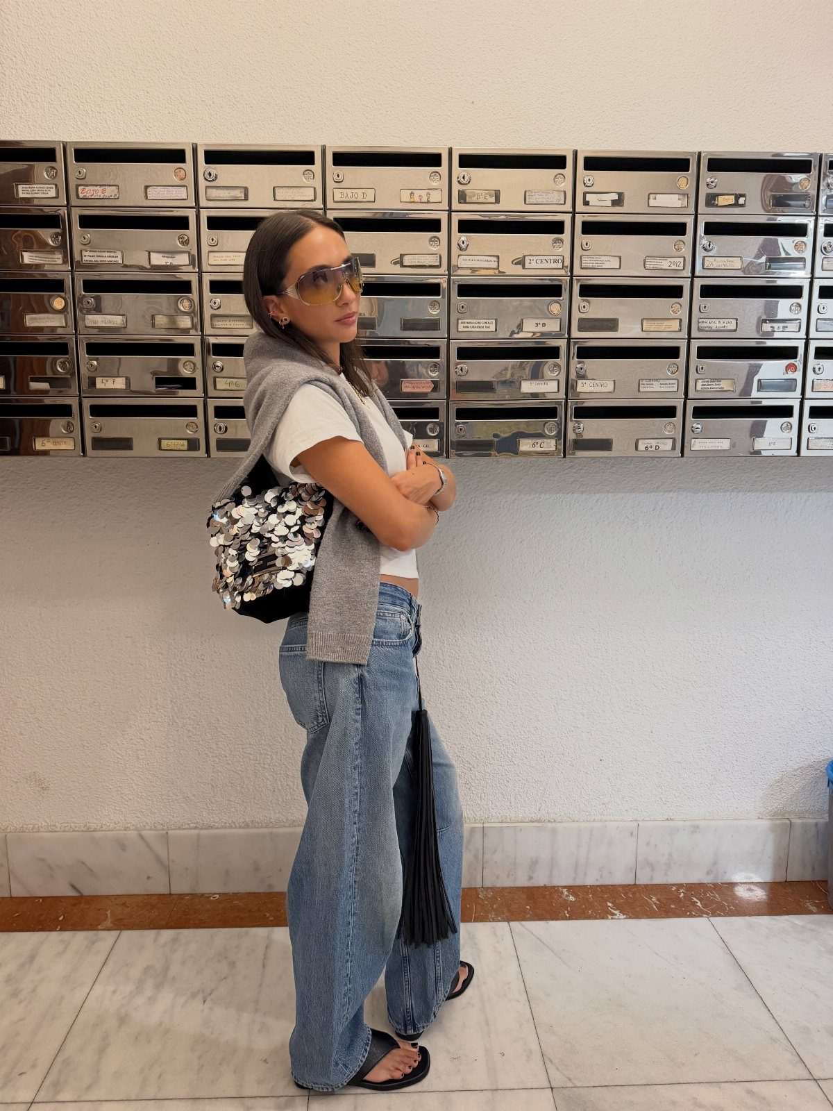 Woman in white t-shirt and wide-leg jeans holding a sequined handbag.