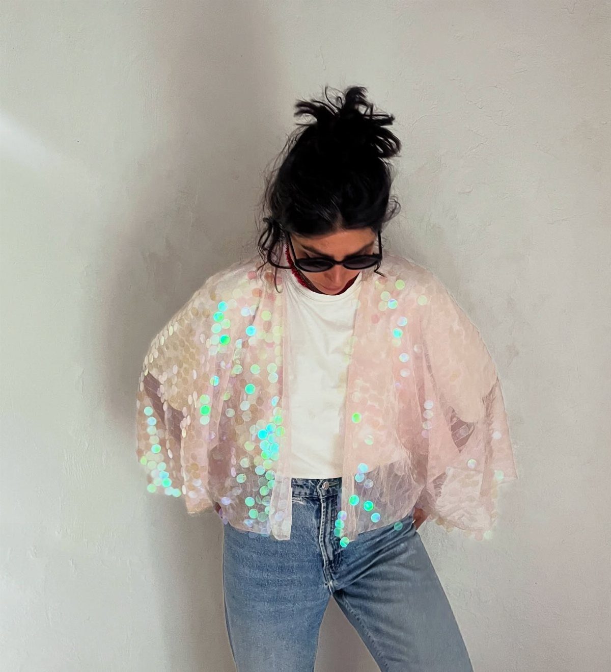 Person wearing a sequined iridescent shrug, white t-shirt, and light blue jeans.