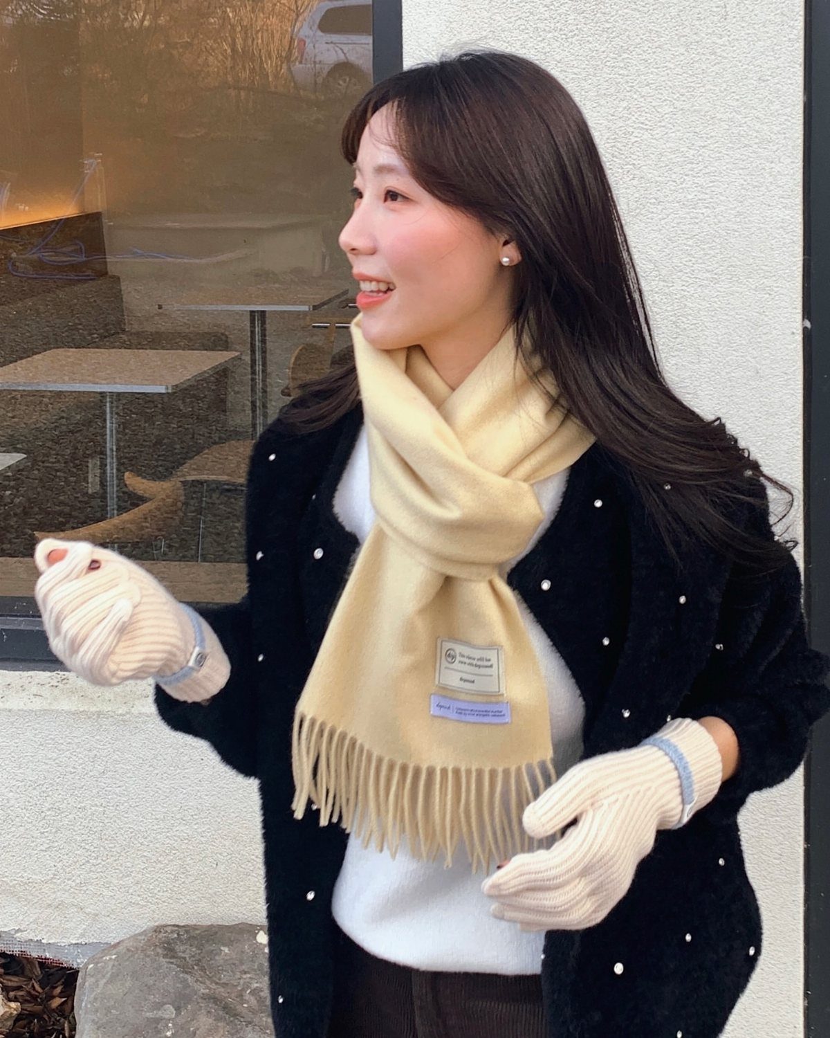 Woman wearing a cream fringed scarf, black dotted cardigan, and matching cream gloves.