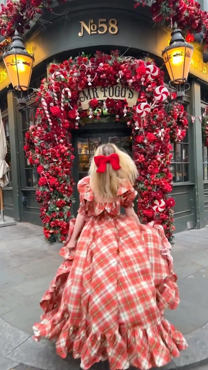 Woman in a long red plaid ruffled gown standing before a festive floral arch.