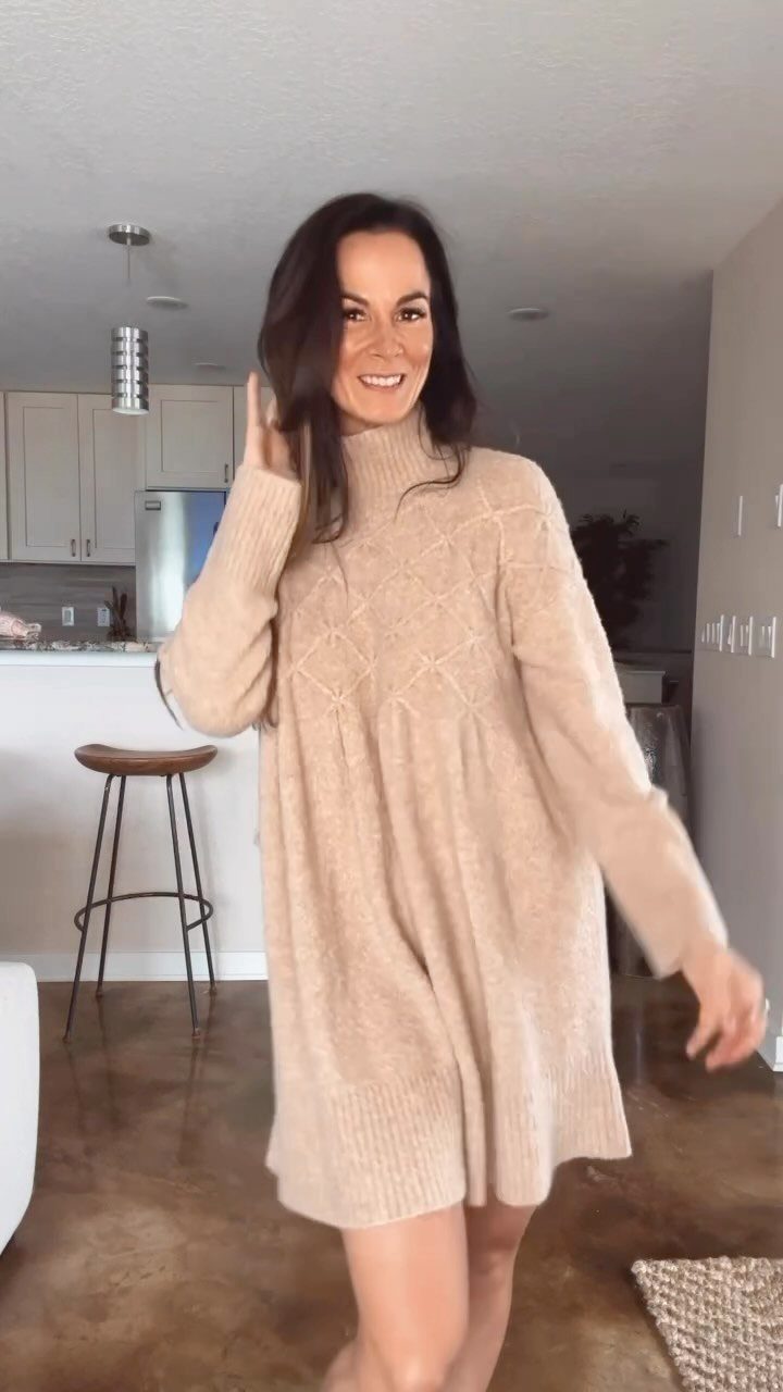 Woman wearing a beige cable-knit sweater dress posing in a modern kitchen setting.
