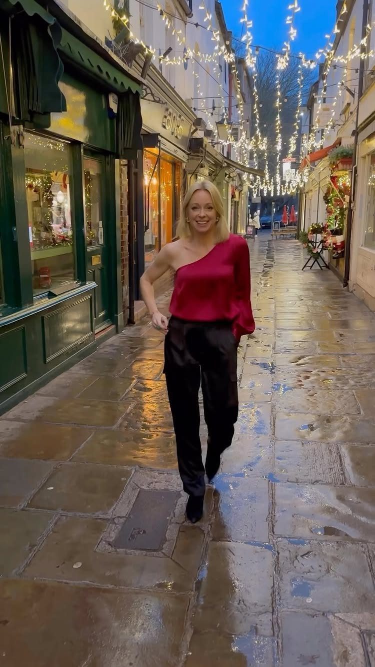 Woman in red satin blouse and black trousers walking on a festive street.