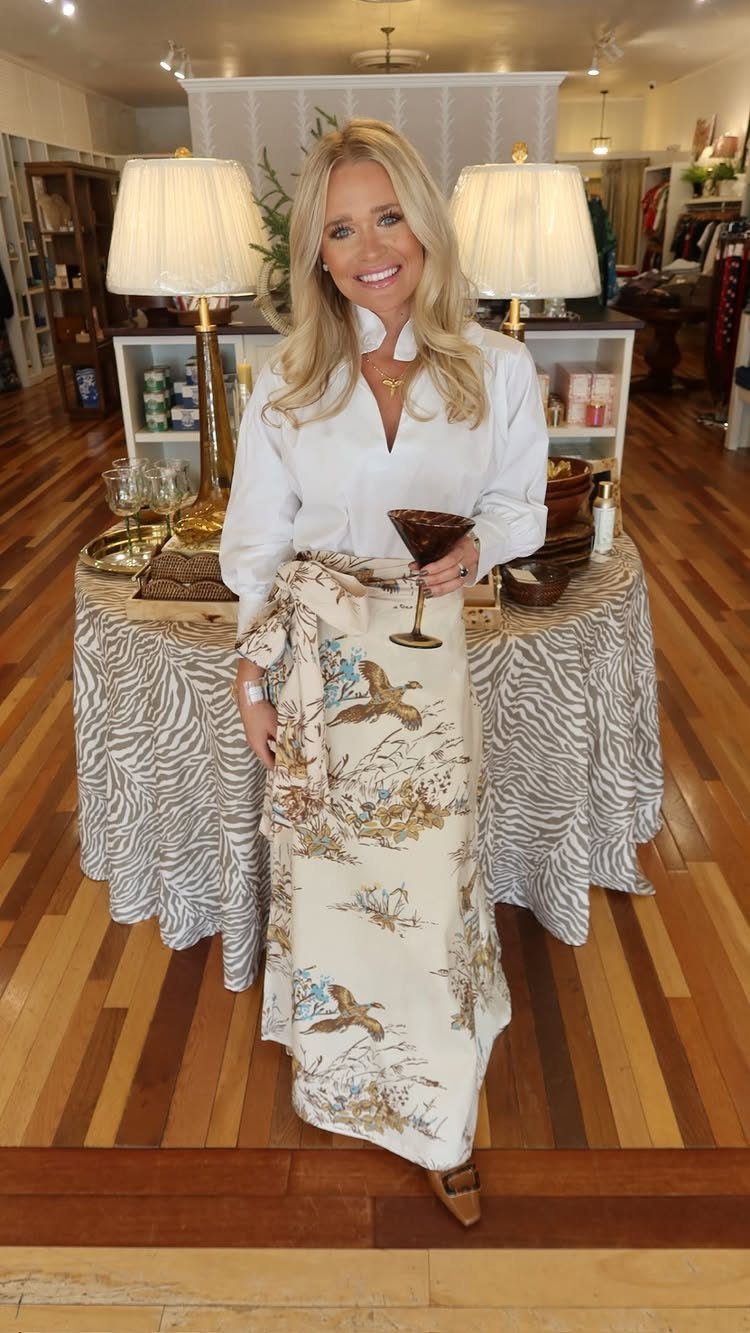 Woman wearing a white button-down blouse and cream bird-print midi skirt holding a cocktail.