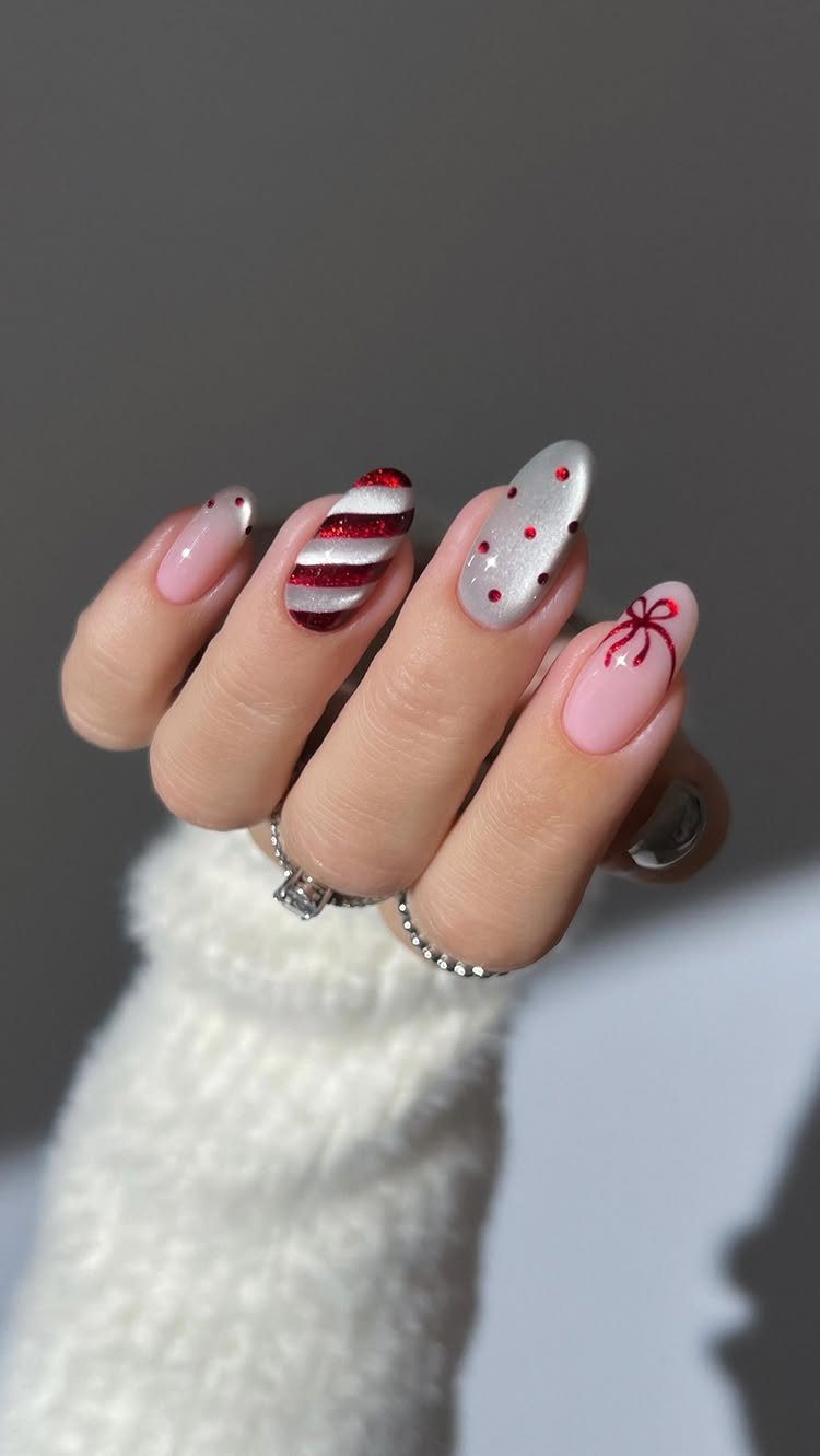 Short oval nails with candy cane stripes, red polka dots, and a red bow.