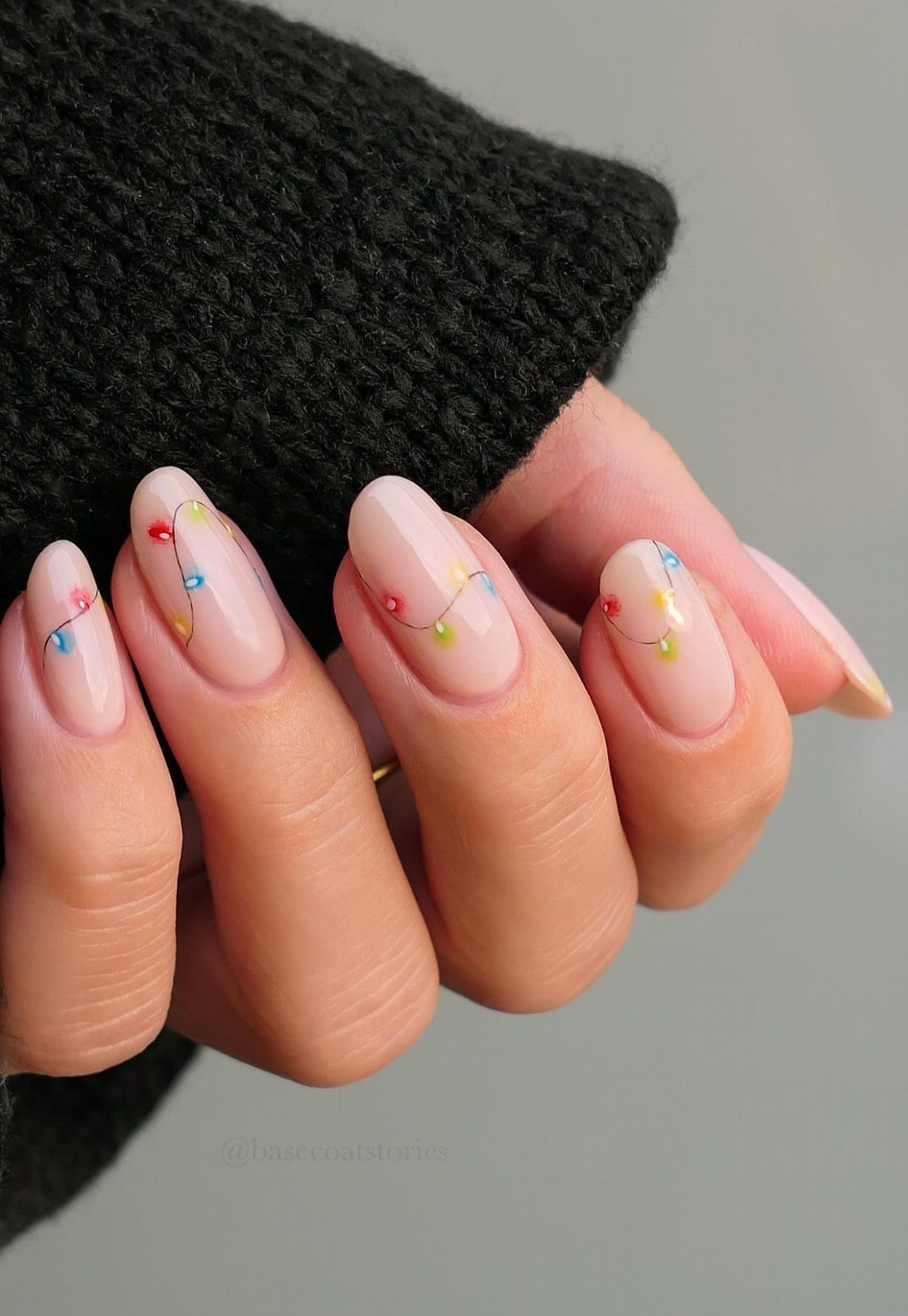 Short nude nails decorated with colorful strings of Christmas lights and a black sweater.