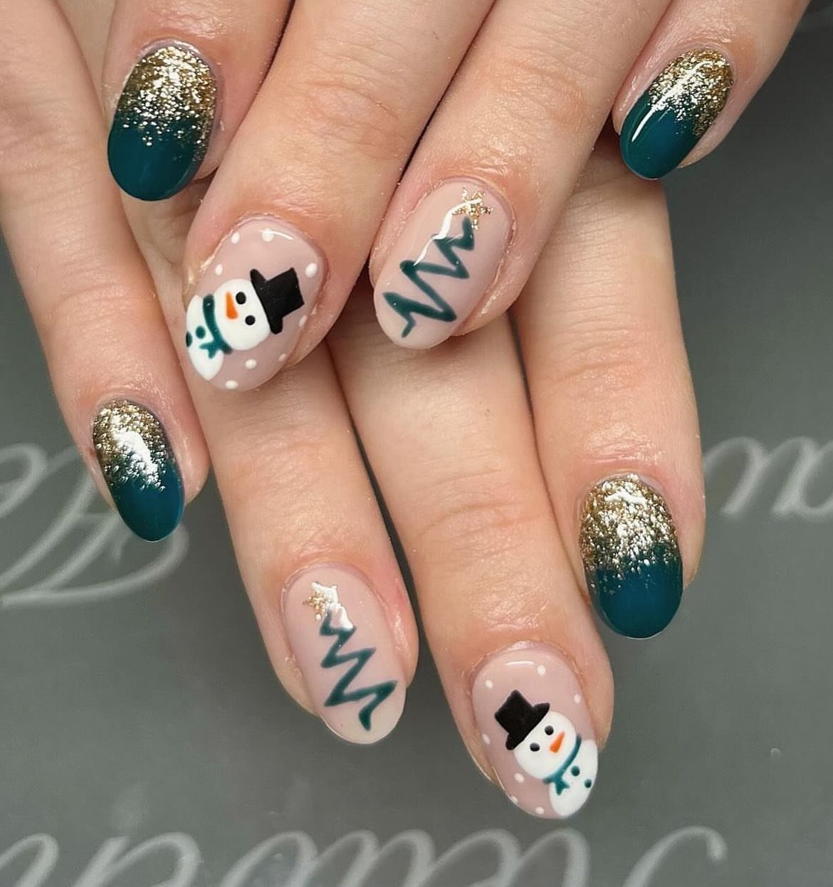 Short nails with Christmas art featuring snowmen, green trees, and gold glitter gradients.