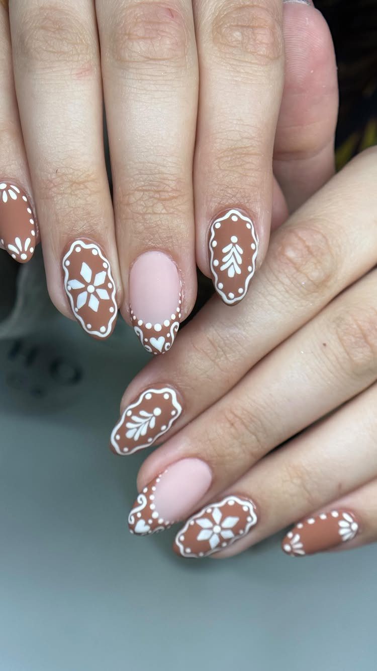 Short nails with brown and pink polish featuring white gingerbread cookie icing patterns.