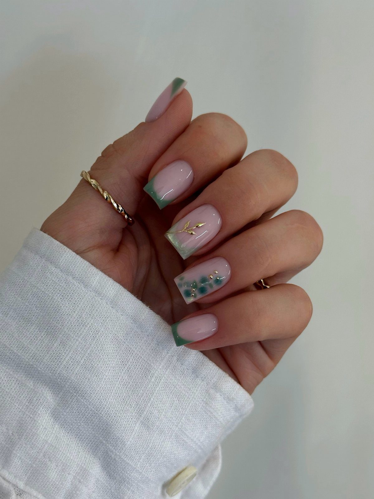 Short almond nails with pale pink polish, green tips, and gold leaf accents.