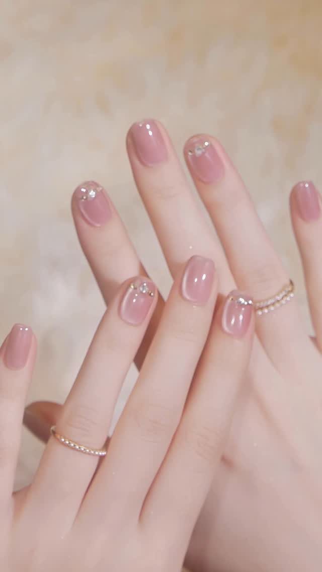 Short light pink nails with small silver rhinestones and gold rings on fingers