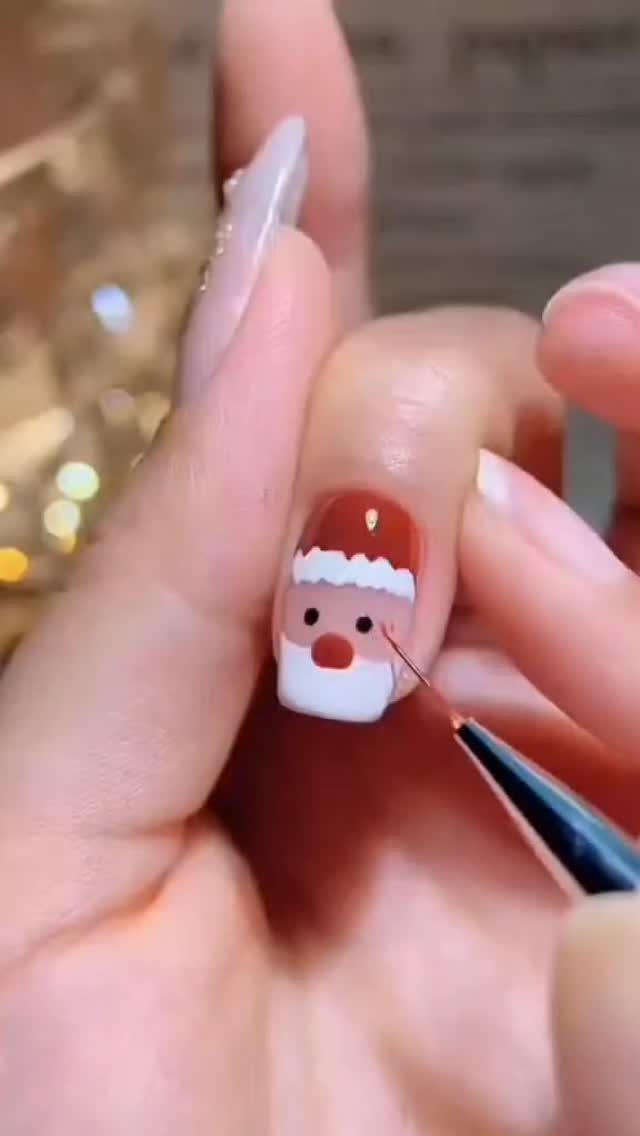 Short fingernail with a Santa Claus design being painted with a fine brush