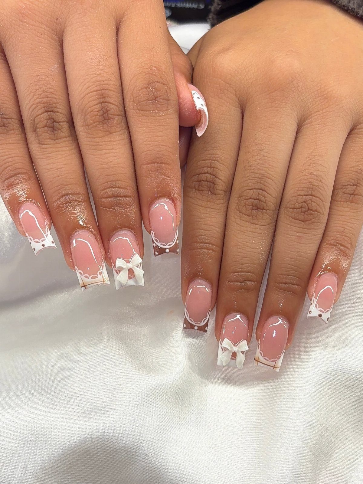 Short almond nails with nude polish and white bow designs on the tips.