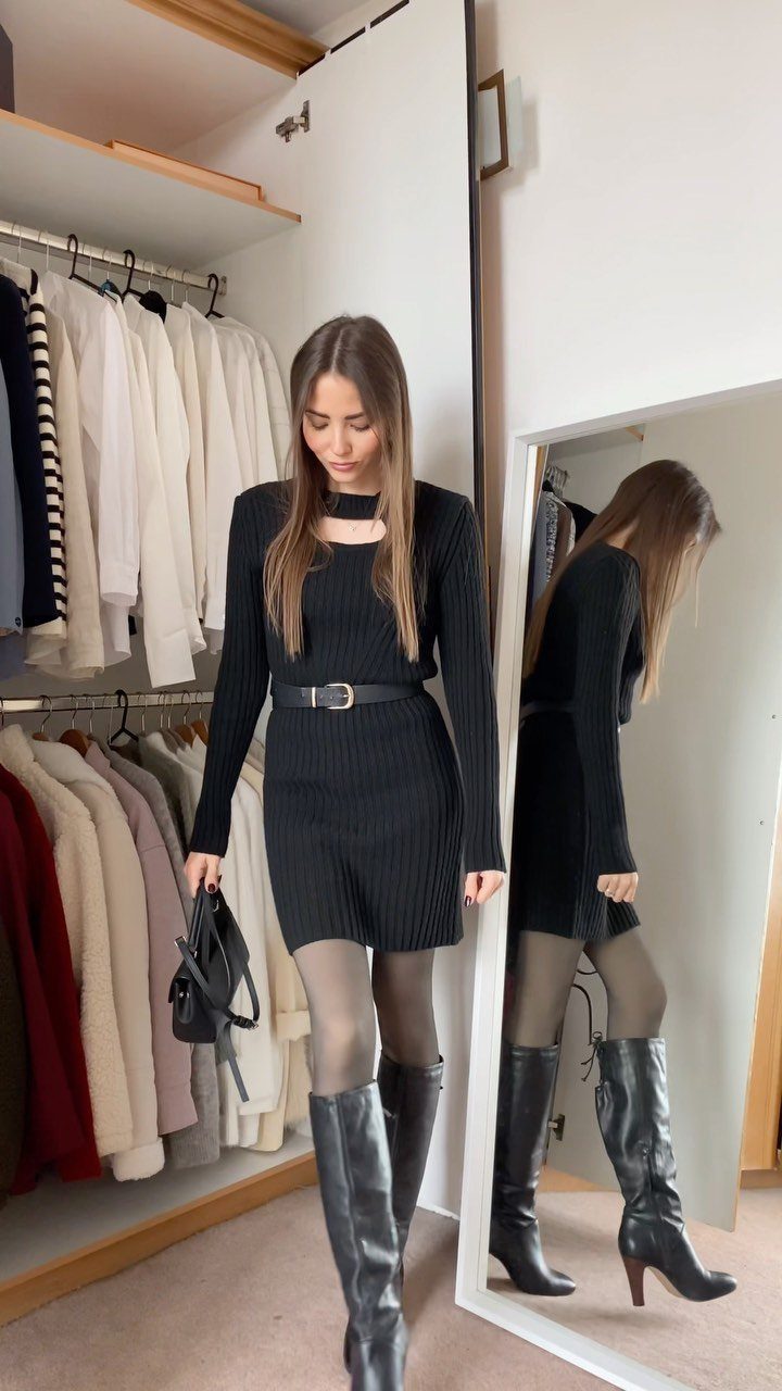 Woman in black sweater dress and knee-high boots posing in a walk-in closet