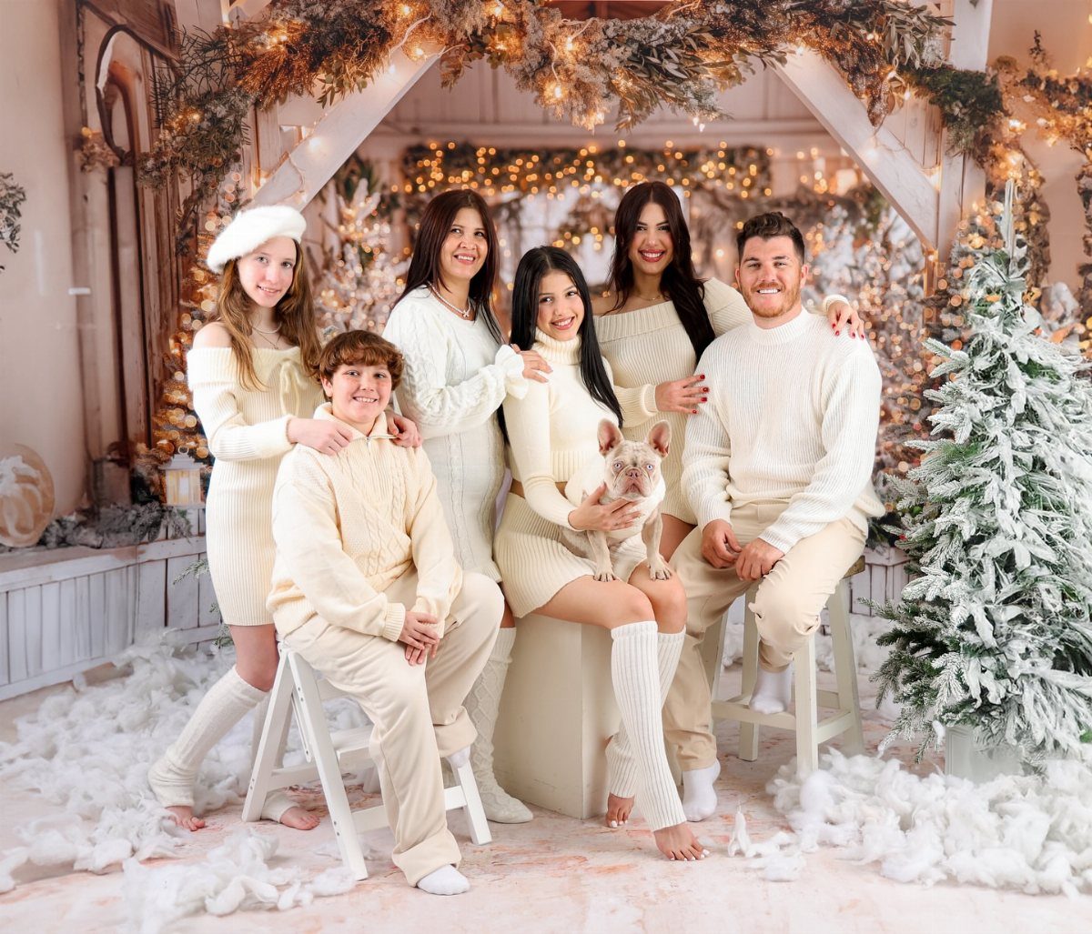 Family in matching cream knit outfits posing in a snowy Christmas studio setting.